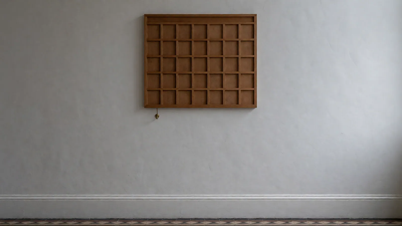 A plain timber calendar board on a chalk-white wall in the hall, its squares empty